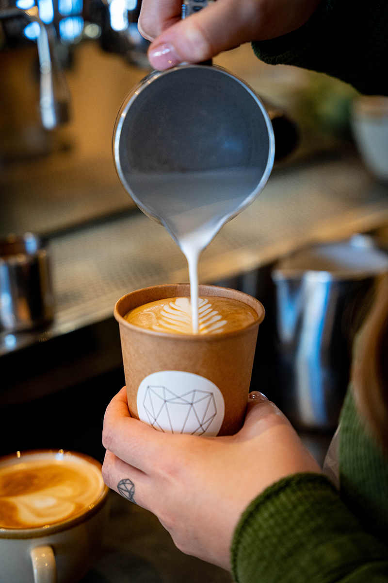 Barista füllt Cappuccionobecher mit Milchschaum und Latte Art im Café Geschwisterherzen Krefeld